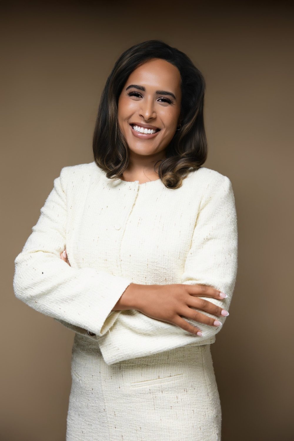 Camille (Cami) Boudreaux, relationship and life coach for women and founder of Fix Your Picker, laughing with her arms crossed in a cream tweed jacket against a warm brown backdrop