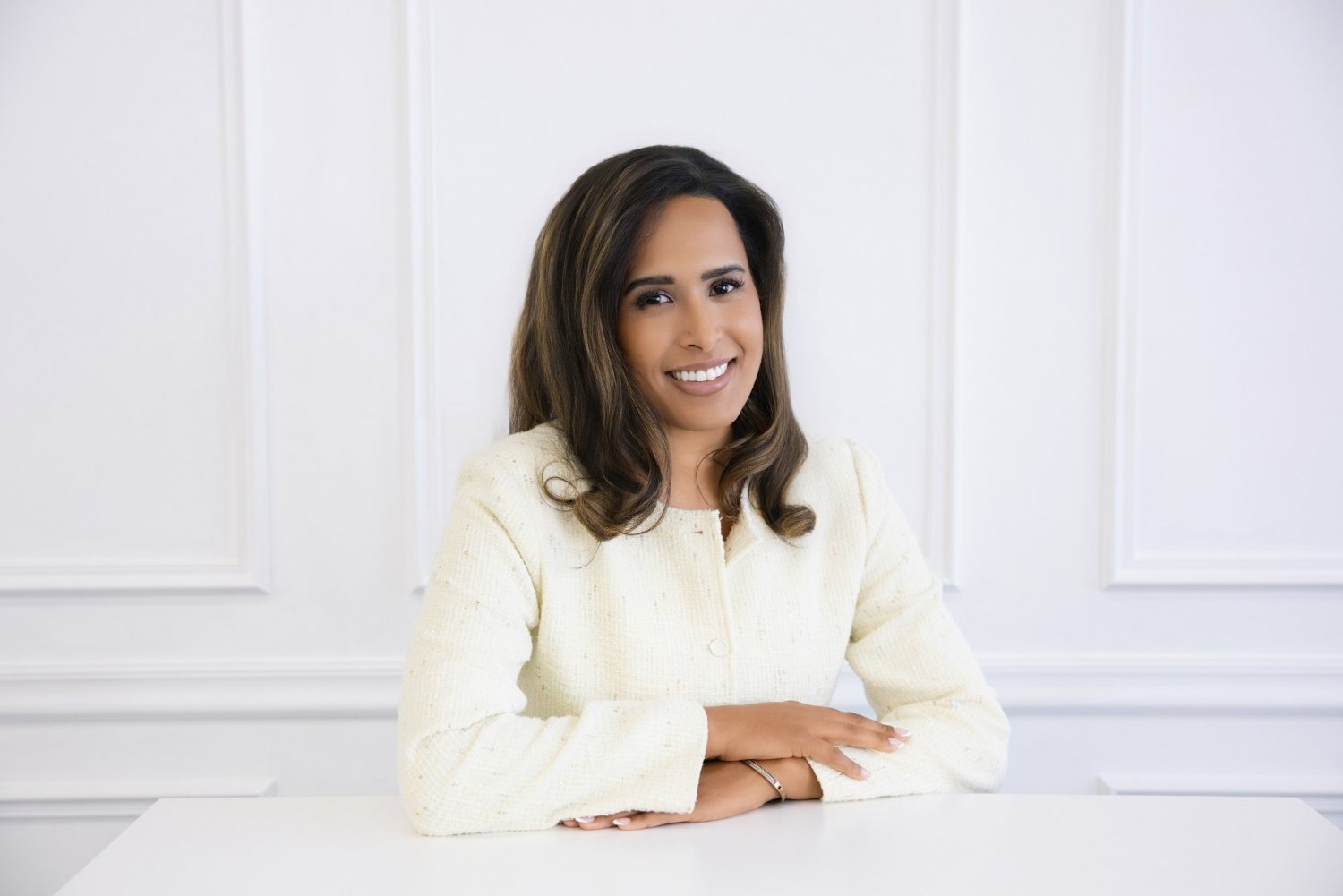 Camille (Cami) Boudreaux, relationship and life coach for women and founder of Fix Your Picker, smiling at a white desk in a cream tweed jacket against white paneled walls