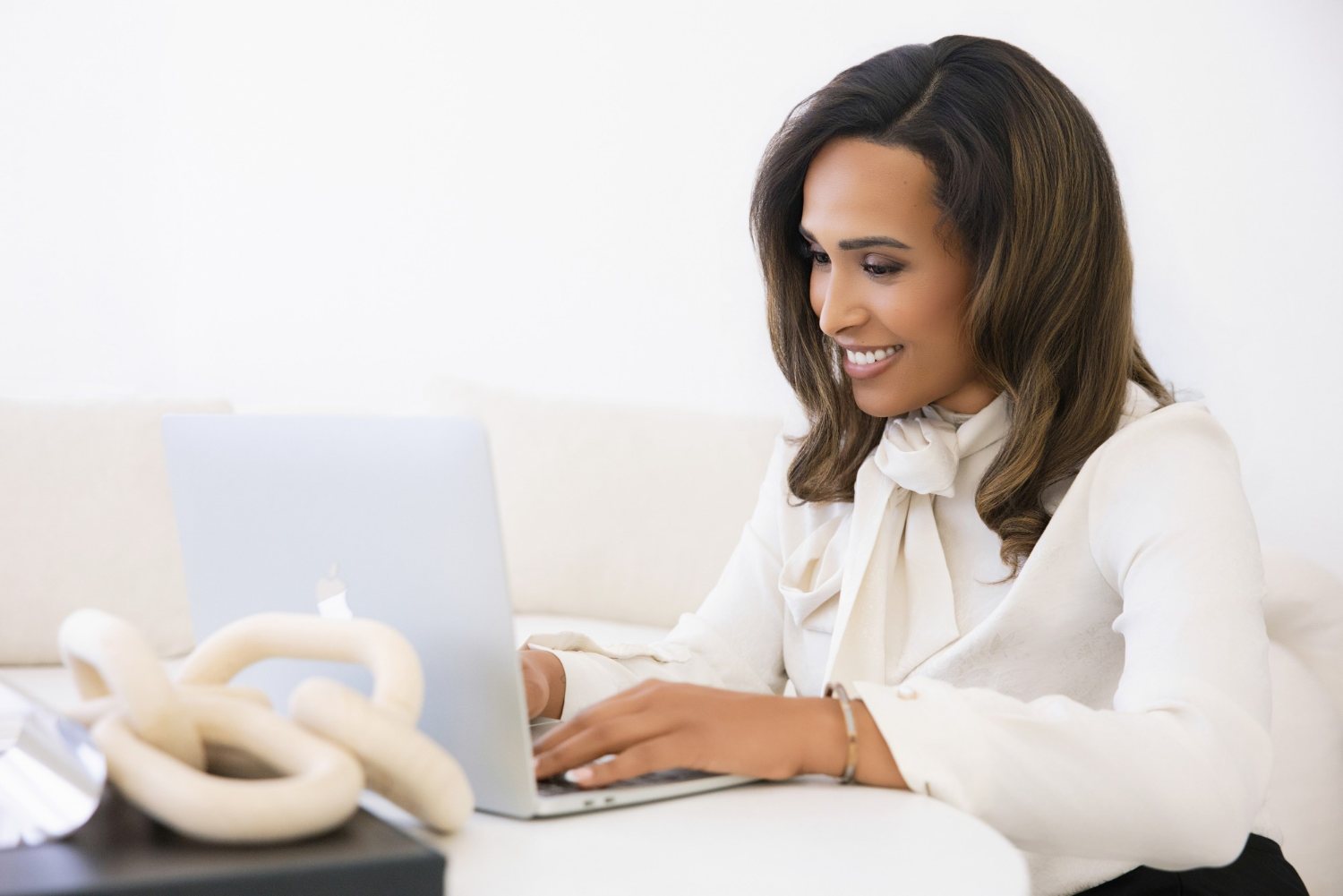 Camille (Cami) Boudreaux, relationship and life coach for women and founder of Fix Your Picker, smiling as she types on her laptop in a white bow-neck blouse
